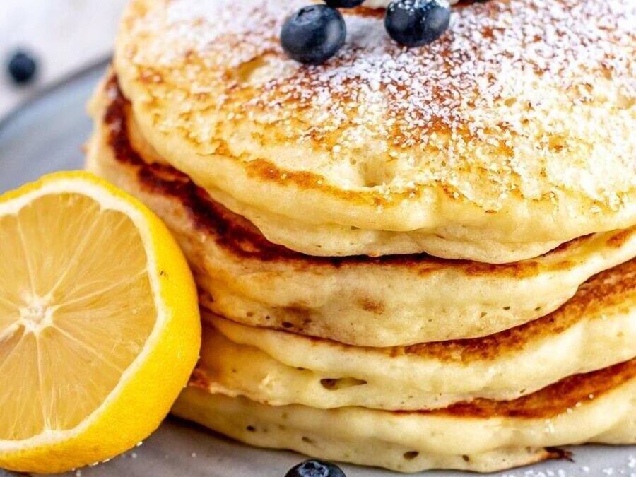 A stack of pancakes with blueberries and lemon slices on a plate.
