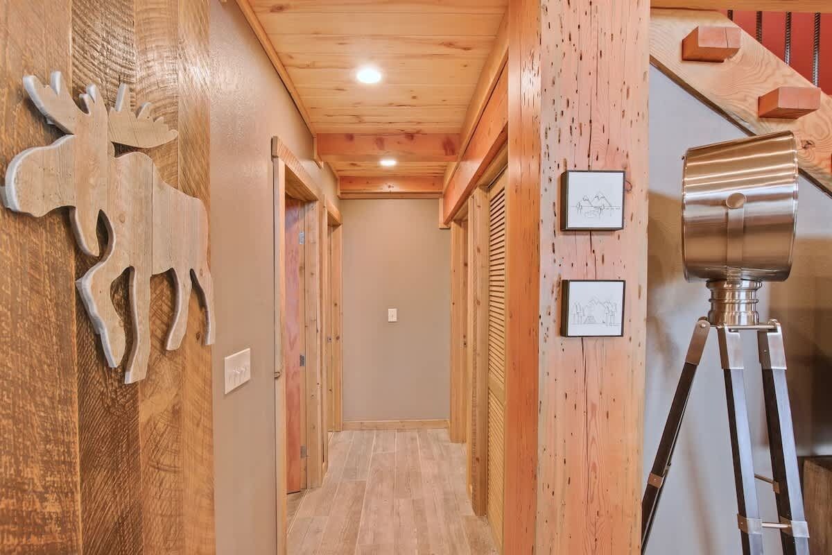 Ein Holzboden-Flur mit einer Holz-Rentiere-Dekoration, gerahmten Bildern an der Wand und einem Stativ.