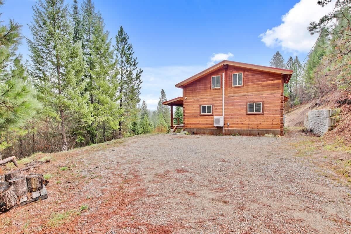 Une cabane en bois à deux étages, avec une allée en gravier, entourée de pins.