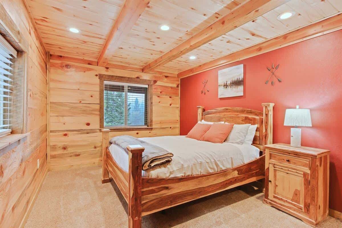 A wooden cabin bedroom with a bed, a nightstand, a window, and a red wall.