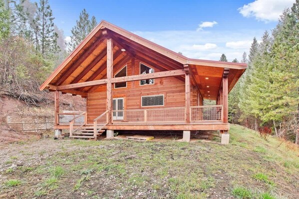 A wooden cabin with a porch, large windows, and a stone wall foundation.