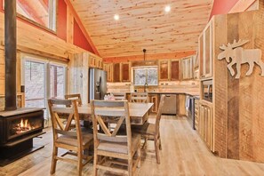 A wooden interior with a fireplace, dining table, chairs, and a kitchen area.