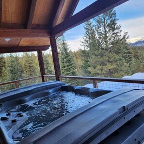 A hot tub with a wooden deck and a view of a forest and mountains.