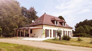 A two-story house with a tiled roof, a covered porch, and a garden in front. - Charming country house in a wooded garden in Perigord Vert (La Coquille)