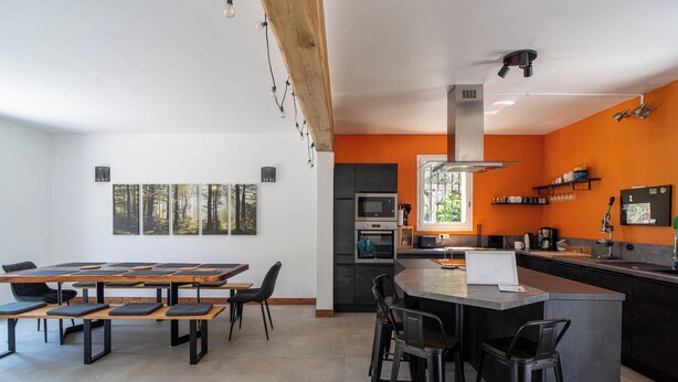 A modern kitchen with a central island, built-in appliances, and a dining area with benches and chairs. - Charming country house in a wooded garden in Perigord Vert (La Coquille)