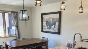 A modern kitchen with a marble countertop, a dining area with a wooden table and chairs, pendant lights, and a framed picture on the wall. - Newly Renovated, 3 bd, 3 bath on shuttle route (Vail)