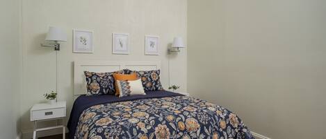 Un dormitorio con cama, mesitas de noche, lámparas de pared y cuadros enmarcados.