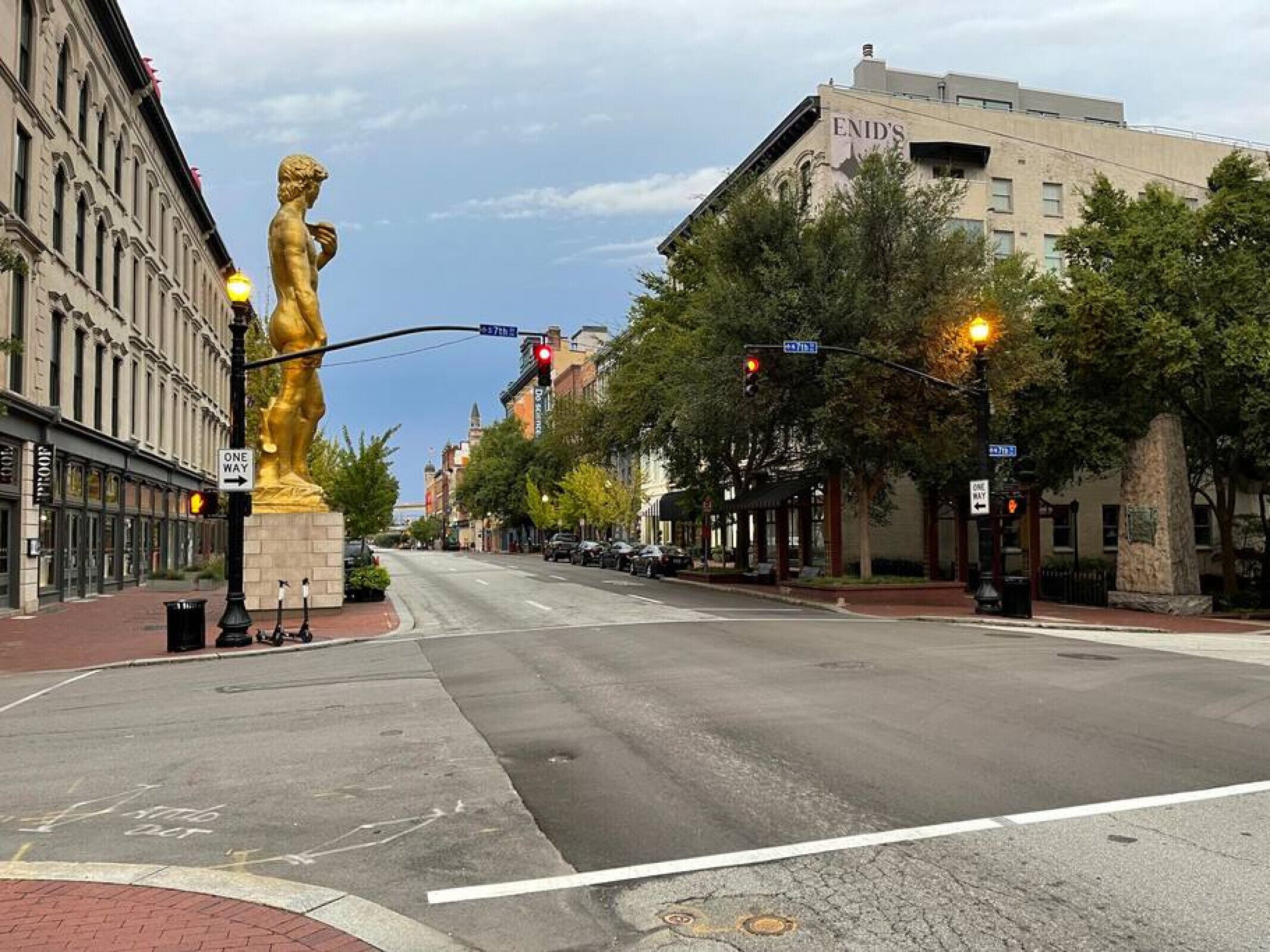 A street with a large golden statue, buildings, and traffic lights.