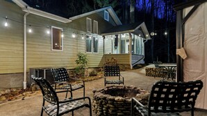 A covered outdoor patio with stone fire pit seating, a table, and chairs.