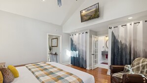 A bedroom with a large bed, a wooden floor, a brown leather chair, and a painting on the wall.