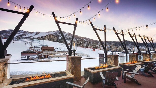 Una terrazza sul tetto con bracieri e poltrone Adirondack che si affaccia su un paesaggio innevato con una pista da sci sullo sfondo.