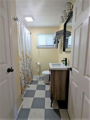 Une petite salle de bain avec un carrelage à motifs géométriques, des toilettes, un lavabo et un rideau de douche orné de motifs floraux.