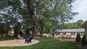 A backyard with a fire pit, two Adirondack chairs, a wooden deck, and a house in the background. - Relax at Moon Dogs Getaway! (Erie)