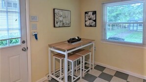 A room with a checkered floor, a small table with a bench, two wall-mounted pictures, a door with a doormat, and a window with blinds. - Relax at Moon Dogs Getaway! (Erie)