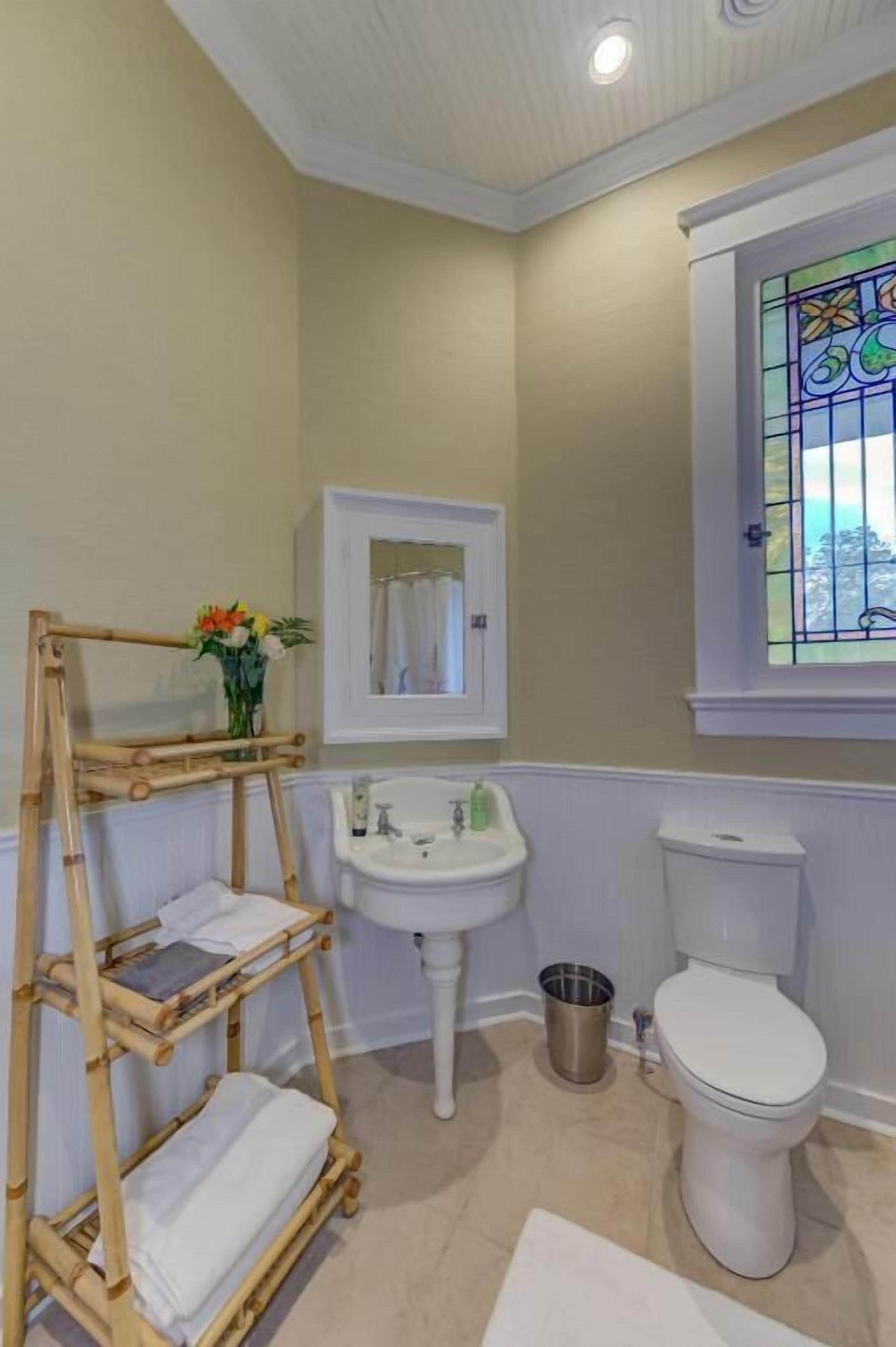 Un baño con lavamanos blanco, inodoro y una ventana con vitral.