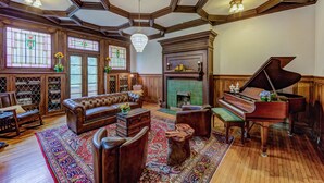 A spacious living room with a grand piano, a fireplace, and a large window with stained glass. - Oak Hall Mansion and Boutique Hotel (Vicksburg)