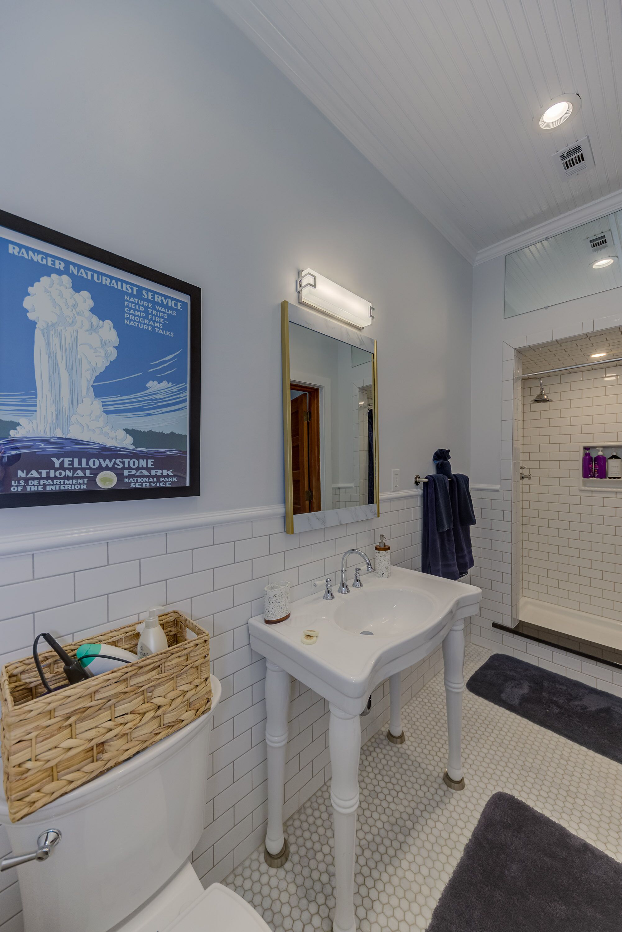 A bathroom with a white sink, a mirror, a shower, and a poster of Yellowstone National Park.