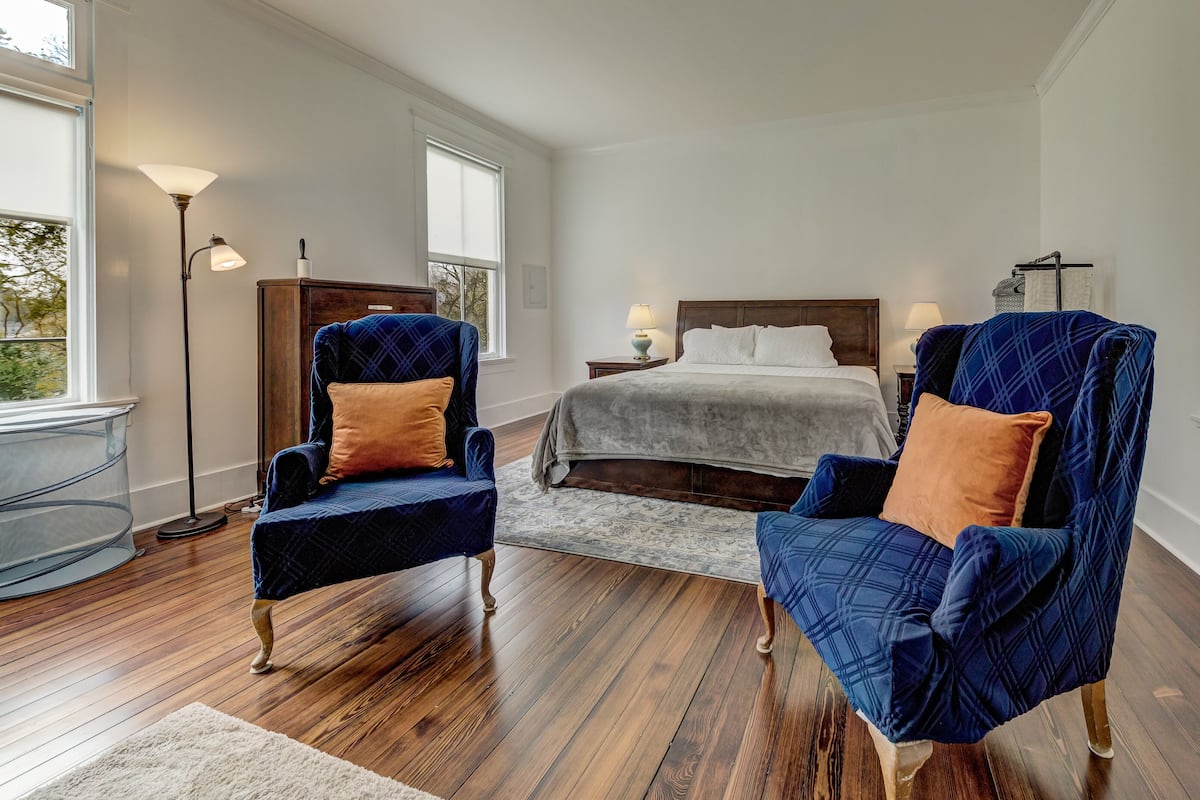 A bedroom with a large bed, two armchairs, a floor lamp, and a window.