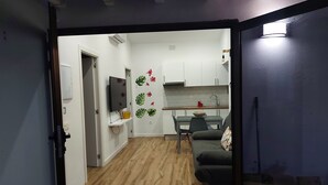 A modern kitchen with white cabinets, a dining table with chairs, and a TV mounted on the wall.