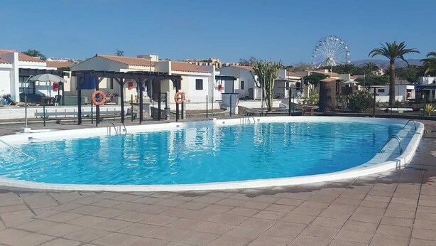 A swimming pool with a clear blue water, surrounded by a tiled deck.