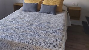 A neatly made bed with a patterned white cover, two bedside tables with lamps, and three abstract wall art pieces above the bed.