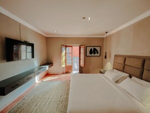 Ein Schlafzimmer mit einem Bett, einem an der Wand befestigten Fernseher, einem Nachttisch und einer Tür, die auf einen Balkon führt.