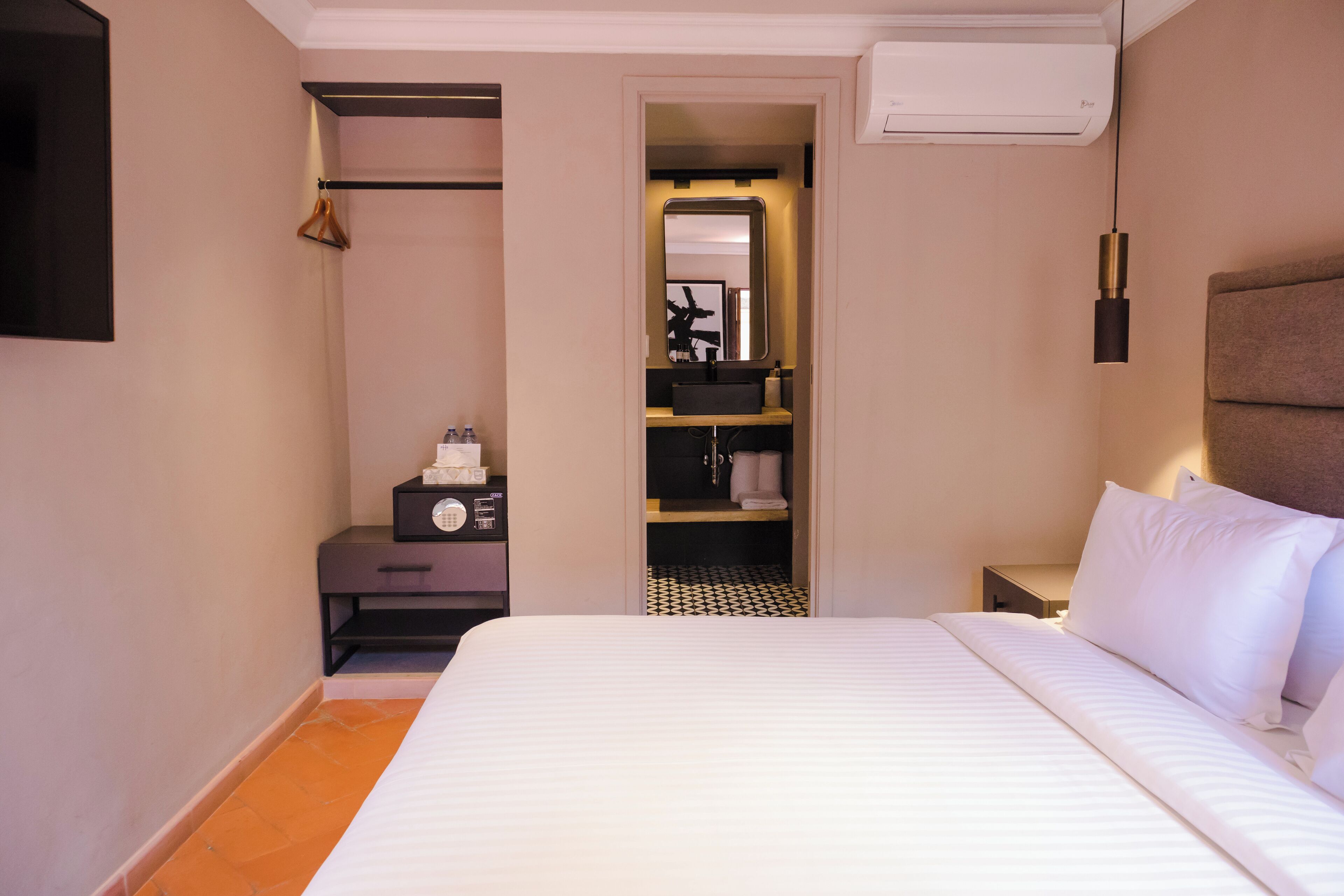 Une chambre d’hôtel comprenant un lit, une armoire, une table de chevet, un miroir et un luminaire suspendu.