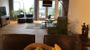 A modern living room with a large TV, comfortable seating, a dining area, and a view of the outdoors.