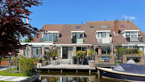 A canal-side house with a dock, a boat, and a garden.