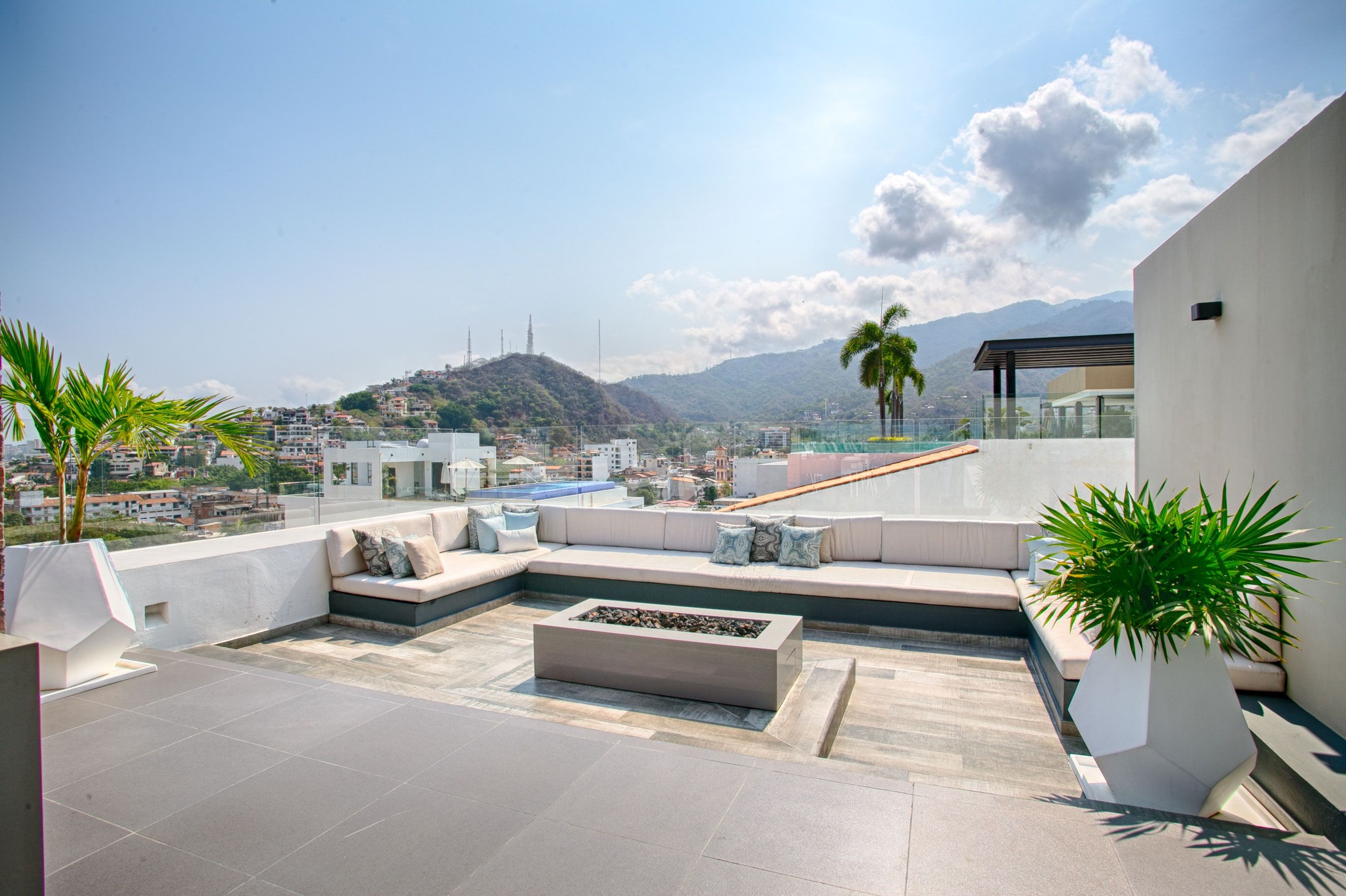 A rooftop terrace with a seating area, a fire pit, and a view of the city and mountains.