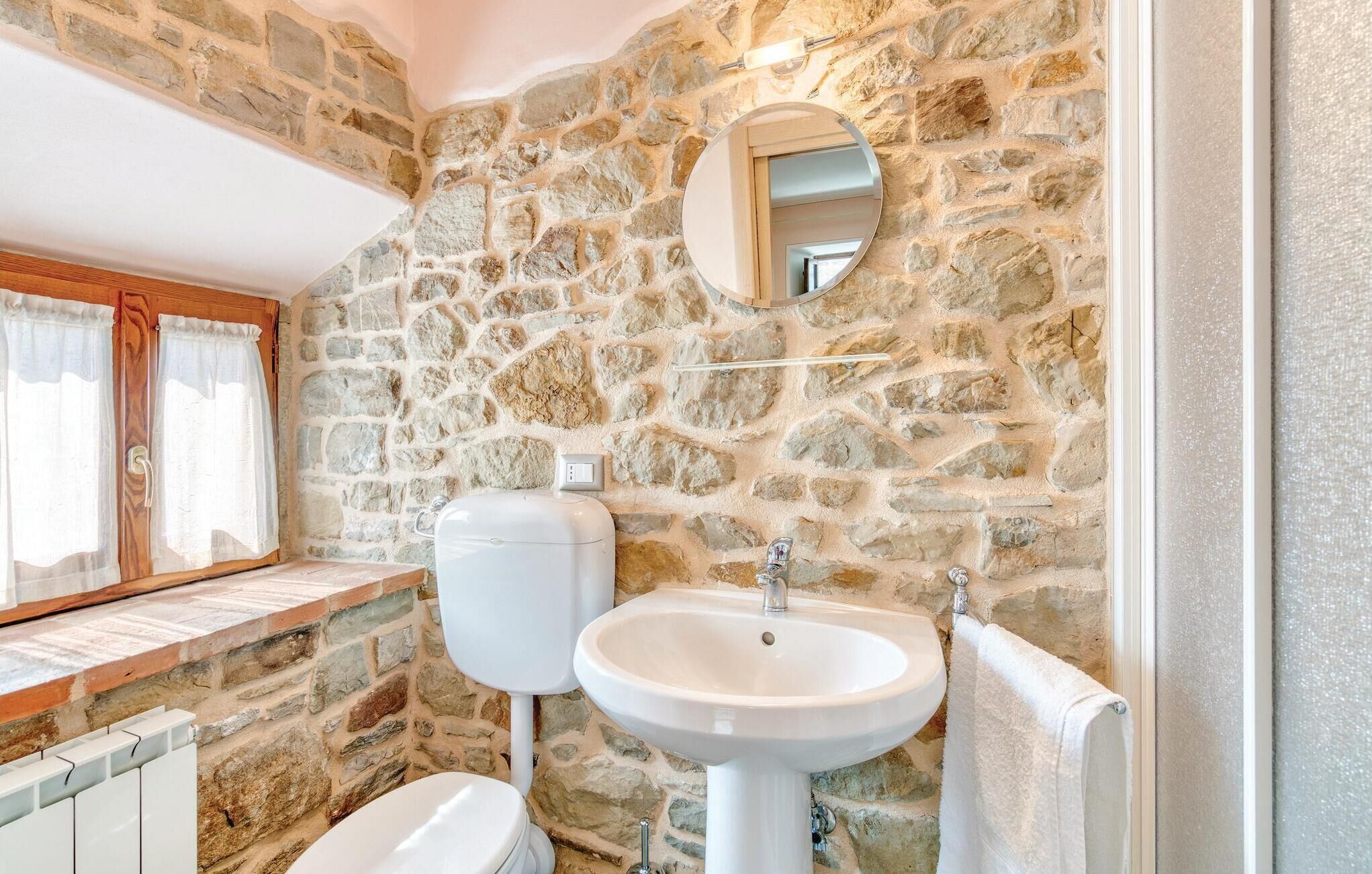 A bathroom with a stone wall, a toilet, a sink, and a mirror.