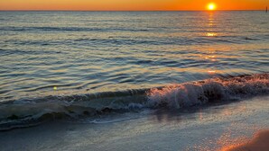 Un coucher de soleil sur une mer calme, où les vagues viennent doucement lécher le rivage.