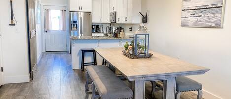 A modern kitchen with white cabinets, a wooden island with benches, a hanging light fixture, and a painting on the wall.