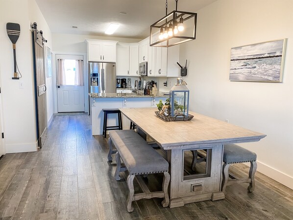 A modern kitchen with white cabinets, a wooden island with benches, a hanging light fixture, and a painting on the wall.