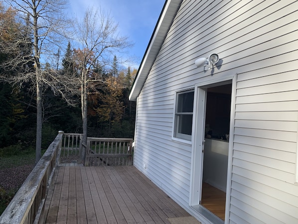 Une terrasse en bois mène à un bâtiment blanc doté d’une porte-fenêtre coulissante.