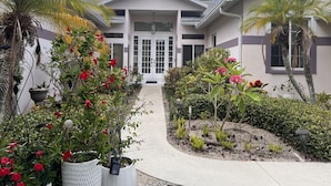 A modern two-story house with a covered patio, surrounded by lush greenery and flowering plants. - :: Villa Oasis – Elegant & Peaceful Pool Retreat in Siesta Key :: (Siesta Key)