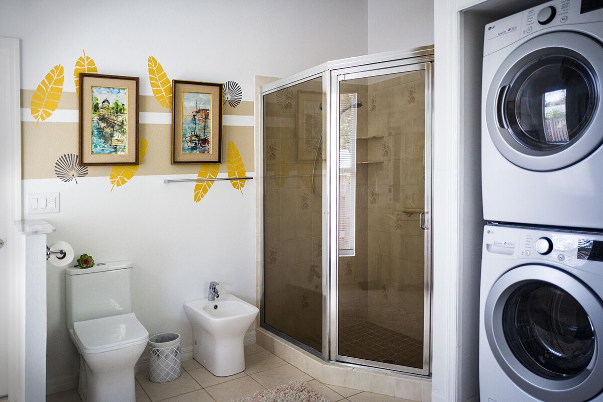 Een compacte badkamer met toilet, bidet en een douchecabine. Twee ingelijste foto's hangen aan de muur en er staat een wasmachine in de hoek.