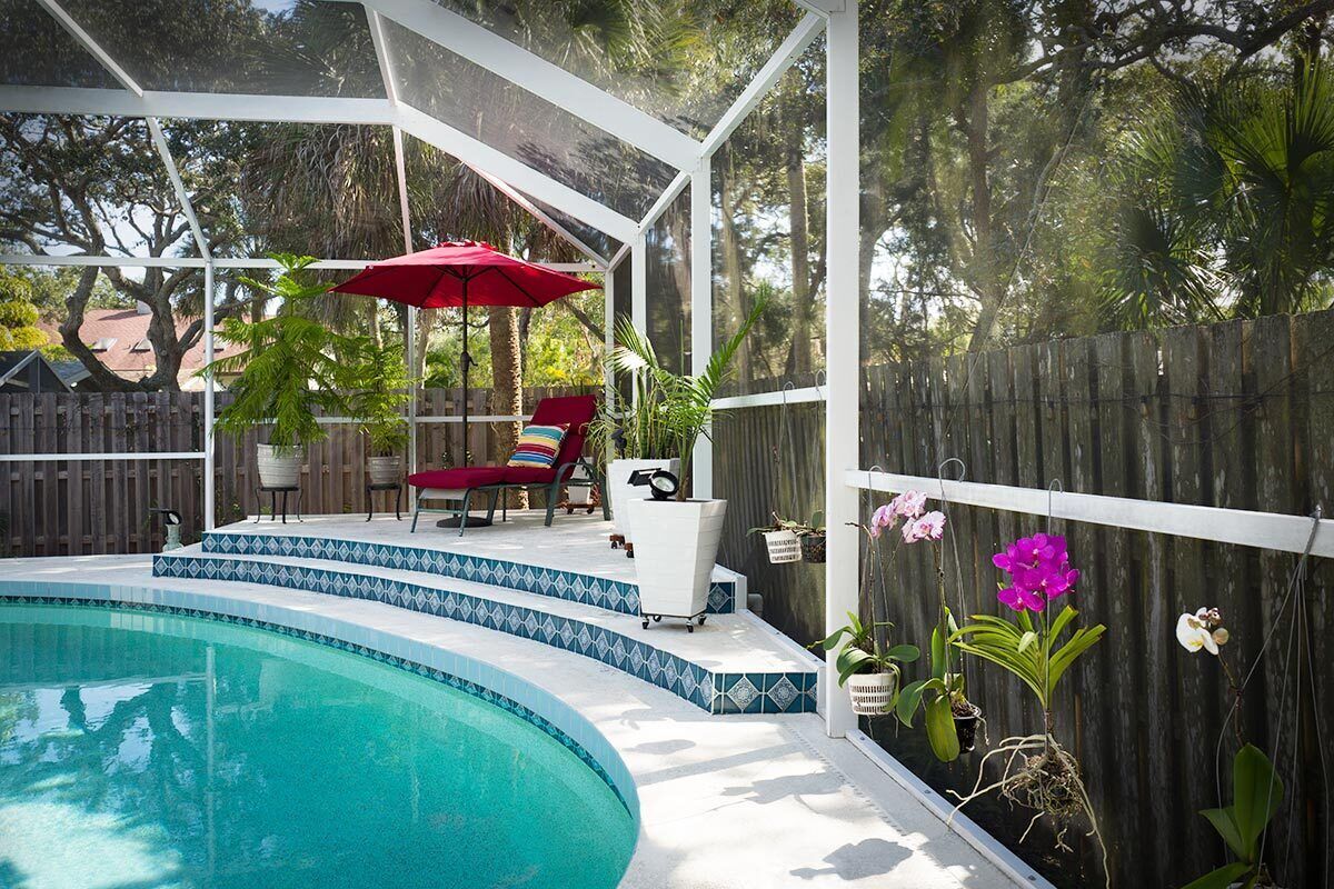 En gårdhave med swimmingpool, en overdækket terrasse med røde stole og plantekrukker.