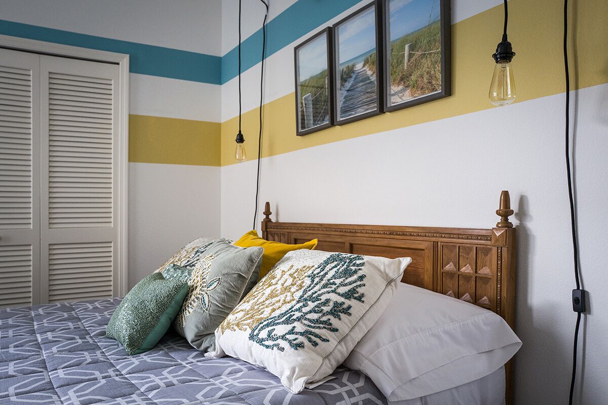 Ein Schlafzimmer mit einem Bett, Kissen, einem hölzernen Kopfteil und einer Wand mit Streifenmuster und gerahmten Bildern.