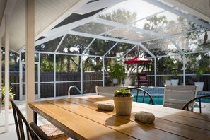 A covered patio area with a wooden table, potted plants, and a pool in the background. - :: Villa Oasis – Elegant & Peaceful Pool Retreat in Siesta Key :: (Siesta Key)
