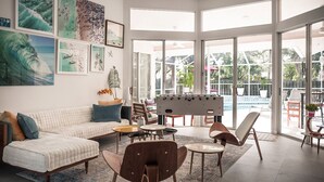 A spacious living area with a sofa, chairs, a foosball table, and large windows overlooking a pool. - :: Villa Oasis – Elegant & Peaceful Pool Retreat in Siesta Key :: (Siesta Key)