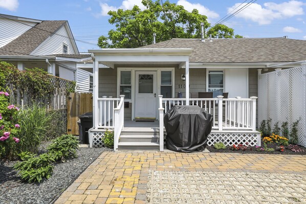 A two-story house with a covered porch, a front door, and a small front yard with plants and a fence.