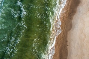 An aerial view of a beach with waves, sand, and a few people.