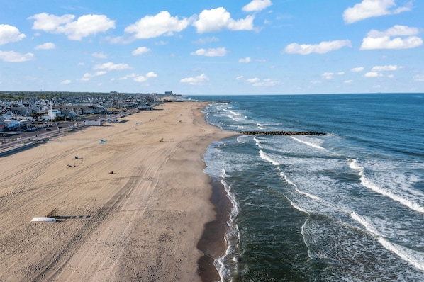A beach with a long stretch of sand, a pier, and a cityscape in the background.