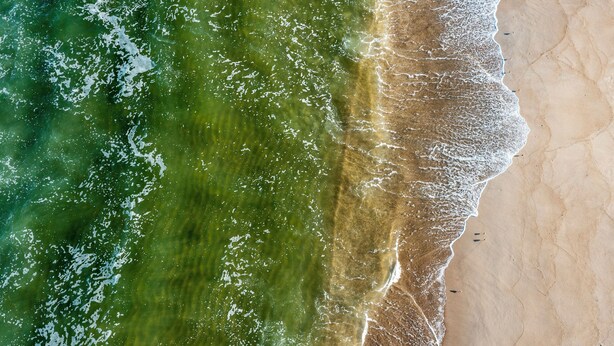 Vue aérienne d’une plage où les vagues déferlent sur le rivage.
