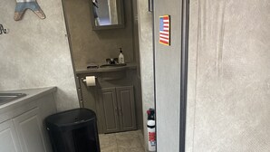 Uma cozinha compacta com pia, lixeira, mesa e uma cadeira, e um extintor de incêndio.