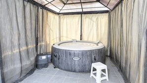 Un bain à remous avec une structure extérieure en bois, un panneau de commande et un tabouret blanc.