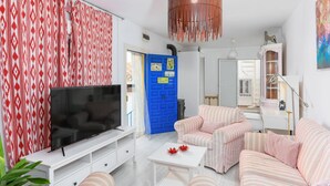 Un salon avec un téléviseur, des canapés à rayures, une porte bleue et un meuble blanc.