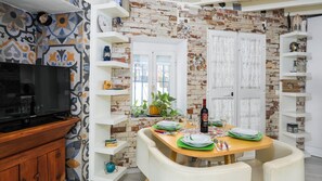 A dining area with a brick wall, white shelves, and a wooden table set for two. - Casa Maruja Cútar by Ruralidays (Málaga)