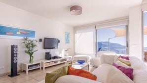 Una sala de estar moderna con televisor de pantalla plana, equipo de sonido, una planta y vistas al exterior.